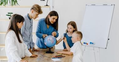Dzieci w szkole uczą się z nauczycielką przy pomocy globusu