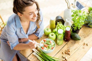 Kobieta siedzi przy stole pełnym warzyw, jedząc sałatkę