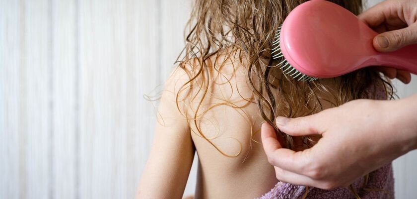 Rodzic rozczesuje dziecku włosy. Pielęgnacja włosów dziecka, jak dbać o włosy dziecka, jak myć włosy dziecku.