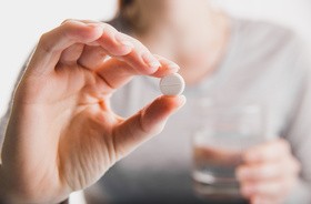 Tabletka przeciwbólowa trzymana miedzy kciukiem a palcem wskazującym