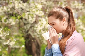 Kobieta, która ma katar alergiczny kicha w chusteczkę, będąc w parku