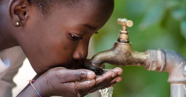 Afrykańskie dziecko pije wodę z ulicznego kranu w złych warunkach sanitarnych narażając się na cholerę