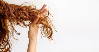 Kosmyk rudobrązowych włosów trzymany przez kobiecą dłoń. Włosy suche, jak dbać o wlosy suche, pielęgnacja włosów suchych.