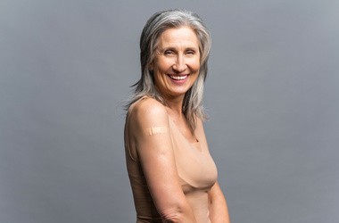 Uśmiechnięta starsza siwowłosa kobieta z plastrem medycznym po szczepieniu
