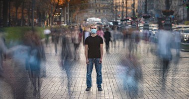 Młody człowiek z maseczką medyczną stoi na zatłoczonej ulicy
