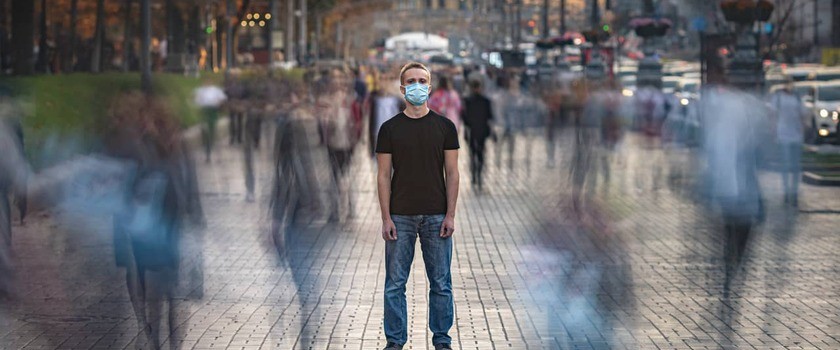 Młody człowiek z maseczką medyczną stoi na zatłoczonej ulicy