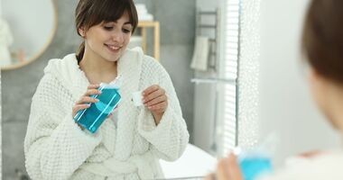 Kobieta płucze jamę ustną przed lustrem. Płukanie ust, płukanie jamy ustnej.