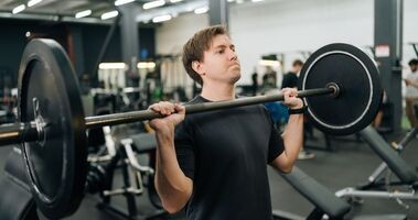 suplementy dla początkujących na siłownię, mężczyzna podnosi sztangę na siłowni
