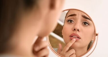 Kobieta przegląda się w lustrze i dotyka ust. Opryszczka wargowa, opryszczka na ustach.