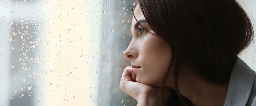 Przygnębiona młoda kobieta w pobliżu okna w domu