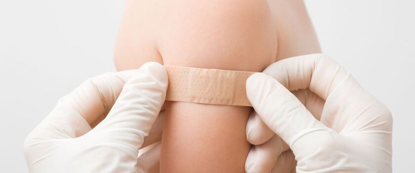 Ręce lekarza naklejające plaster po szczepieniu na ramię. NOP, niepożądany odczyn poszczepienny. 