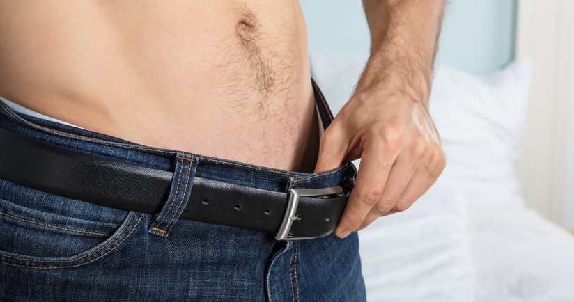 Zabieg wazektomii, wazektomia. Zbliżenie na męskie podbrzusze, mężczyzna bez koszulki odchyla pasek od spodni.