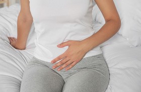 Zapalenie układu moczowego u kobiety siedzącej na łóżku i cierpiącej