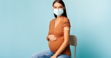 Kobieta w ciąży siedzi na krześle i ma maseczkę na twarzy