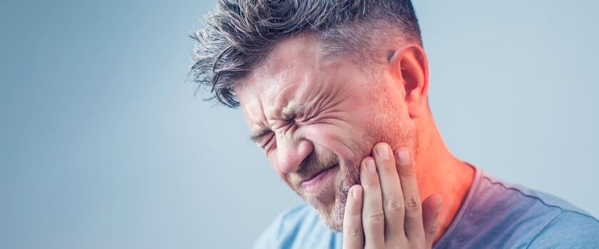 Mężczyzna trzyma się za bolącą twarz, czując ból zęba