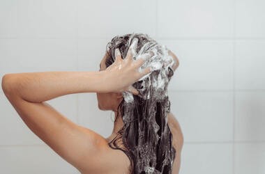 Kobieta wciera pod prysznicem szampon na suchą skórę głowy