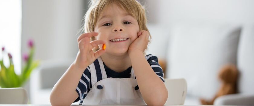 dziecko z witaminą w ręku, suplementy i witaminy na odporność, jak uniknąć infekcji