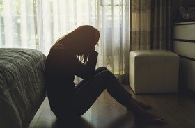 Samotna młoda kobieta czuje się przygnębiona i zestresowana, siedzi w ciemnej sypialni