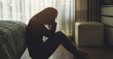 Samotna młoda kobieta czuje się przygnębiona i zestresowana, siedzi w ciemnej sypialni