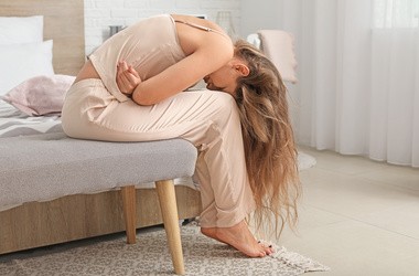 Kobieta siedzi na łóżku, odczuwając ból menstruacyjny. Ból e endometriozie
