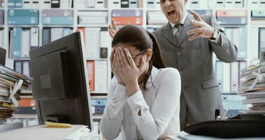 Przykład mobbingu: szef krzyczy na pracownicę siedzącą przy biurku
