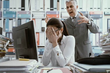 Przykład mobbingu: szef krzyczy na pracownicę siedzącą przy biurku