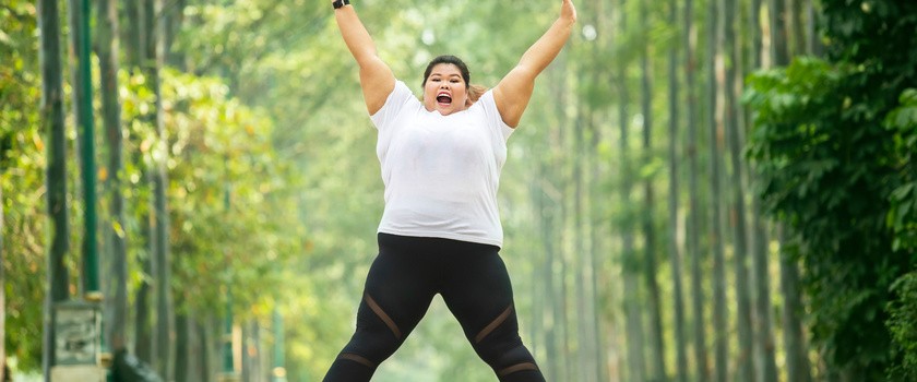 Zadowolona, otyła kobieta skacze do góry podczas biegania w parku