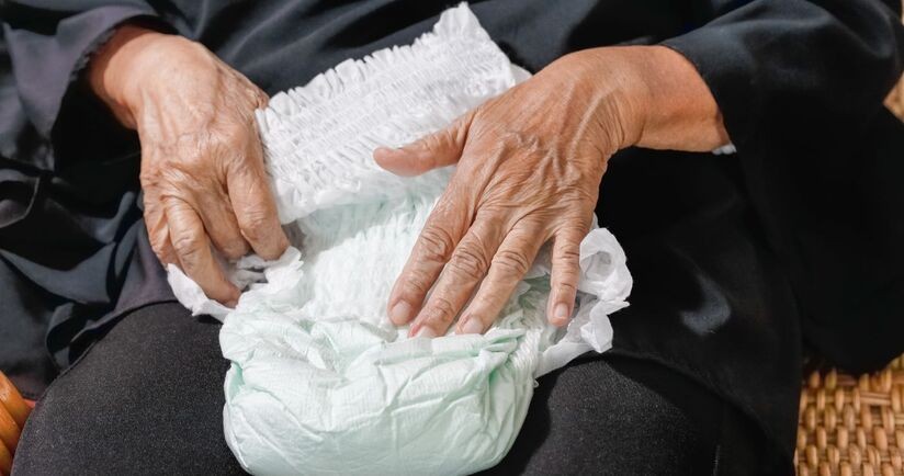 Starsza osoba trzymająca pieluchomajtki dla dorosłych. Inkontynencja kałowa, nietrzymanie stolca.