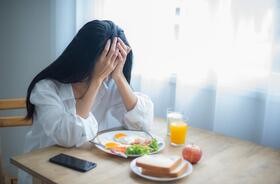 Młoda kobieta siedzi smutna przy stole, na którym stoi talerz pełen smacznych potraw