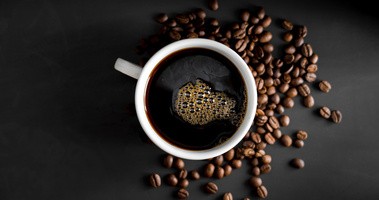 Filiżanka gorącej kawy na tle rozsypanych ziaren kawy na czarnym tle