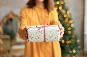 Kobieta z prezentem na tle choinki. Prezent dla rodziców na Święta, prezent dla teściów na Święta, prezent dla mamy, prezent dla taty, prezent dla teścia, prezent dla teściowej.