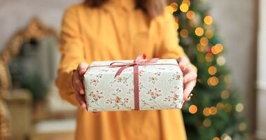 Kobieta z prezentem na tle choinki. Prezent dla rodziców na Święta, prezent dla teściów na Święta, prezent dla mamy, prezent dla taty, prezent dla teścia, prezent dla teściowej.