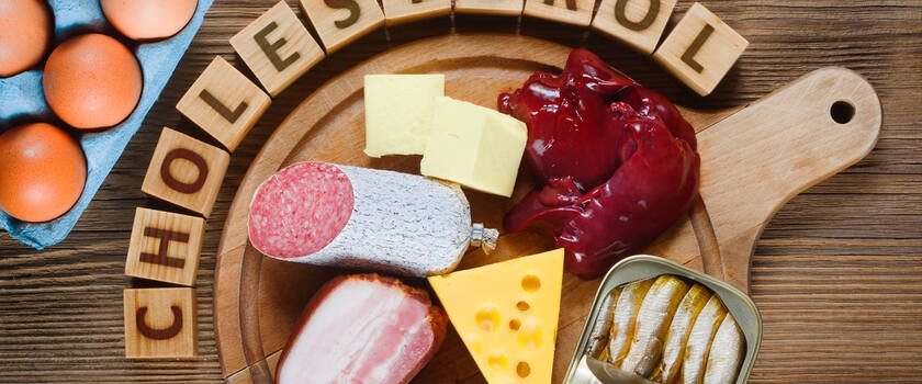 Niedrowe, tłuste produkty, które podwyższaja poziom cholesterolu, leżą na drewnianytm stole.