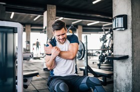 Mężczyzna ćwiczący na siłowni trzyma się za ramię z powodu bólu naderwanego mięśnia