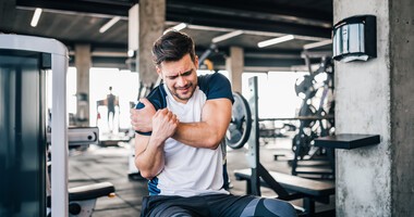 Mężczyzna ćwiczący na siłowni trzyma się za ramię z powodu bólu naderwanego mięśnia