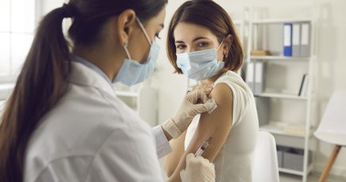 Młoda kobieta w masce na twarz dostaje w szpitalu szczepionkę przeciwko koronawirusowi