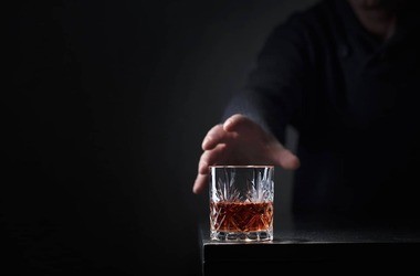 mężczyzna sięga po szklankę z alkoholem
