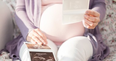 Kobieta w ciąży siedzi z wynikami badania USG, trzymając je przed sobą