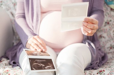 Kobieta w ciąży siedzi z wynikami badania USG, trzymając je przed sobą