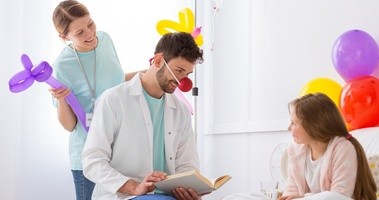 Doktor w stroju klauna stouje terapię śmiechem przy szpitalnym łóżku dziewczynki