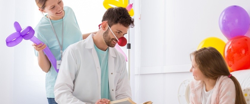 Doktor w stroju klauna stouje terapię śmiechem przy szpitalnym łóżku dziewczynki