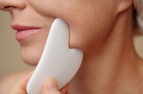 gua sha, masaż gua sha, kobieta wykonująca masaż twarzy kamieniem gua sha