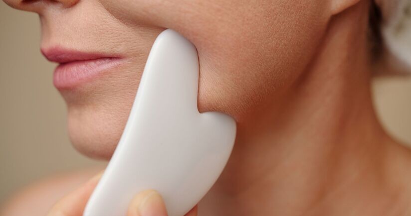 gua sha, masaż gua sha, kobieta wykonująca masaż twarzy kamieniem gua sha