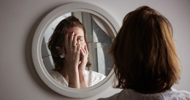 Kobieta patrzy w potłuczone lustro, jako obraz rozdwojenia osobowości obserwowany w schizofrenii